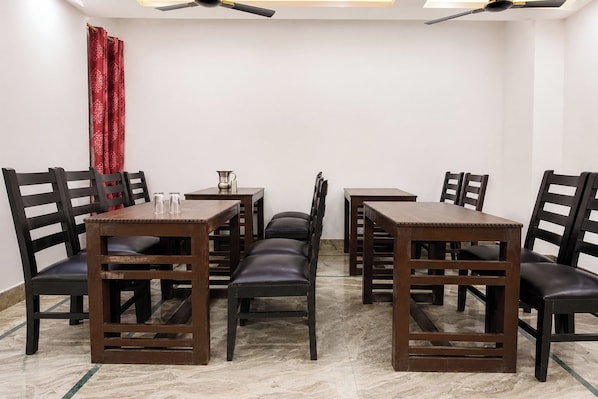 A dining area with a marble floor, wooden tables and chairs, and a ceiling fan. - FabHotel Maharaja Palace (Haridwar)