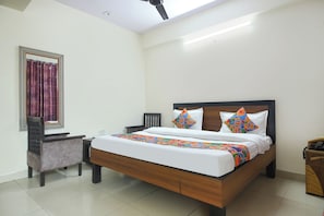 A hotel room with a bed, a chair, a nightstand, a mirror, and a ceiling fan. - FabHotel Maharaja Palace (Haridwar)