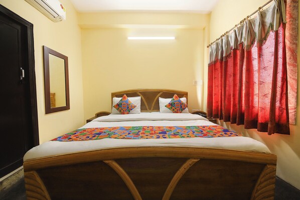 Una habitación de hotel con cama, espejo, ventana con cortinas y aire acondicionado.
