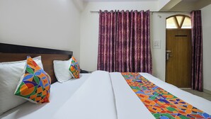 Una habitación de hotel con cama, cabecero, ventana con cortinas y una puerta.