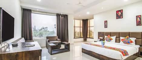 A hotel room with a bed, a desk, a chair, a TV, and a window with curtains.