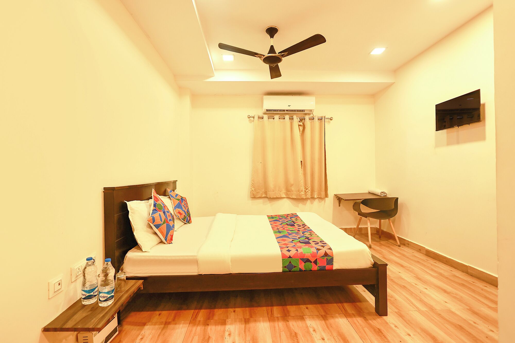 A bedroom with a bed, a ceiling fan, an air conditioning unit, a desk, and a chair.