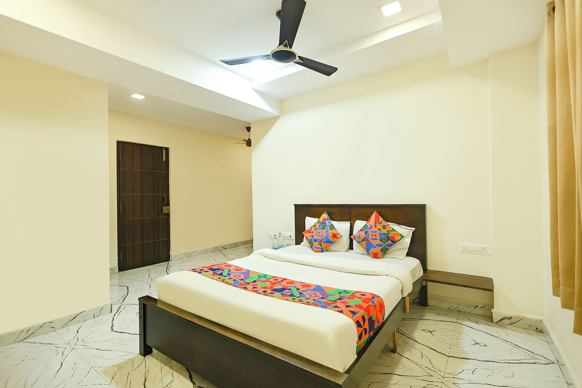 A hotel room with a bed, a ceiling fan, a nightstand, and a door.