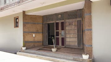 A building entrance with a metal gate, two potted plants on the steps, and a sign reading 'Singh House'.