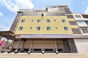 A multi-story building with a yellow facade, multiple windows, and a covered entrance area with potted plants. - FabHotel Prime Garvit (Jaipur)