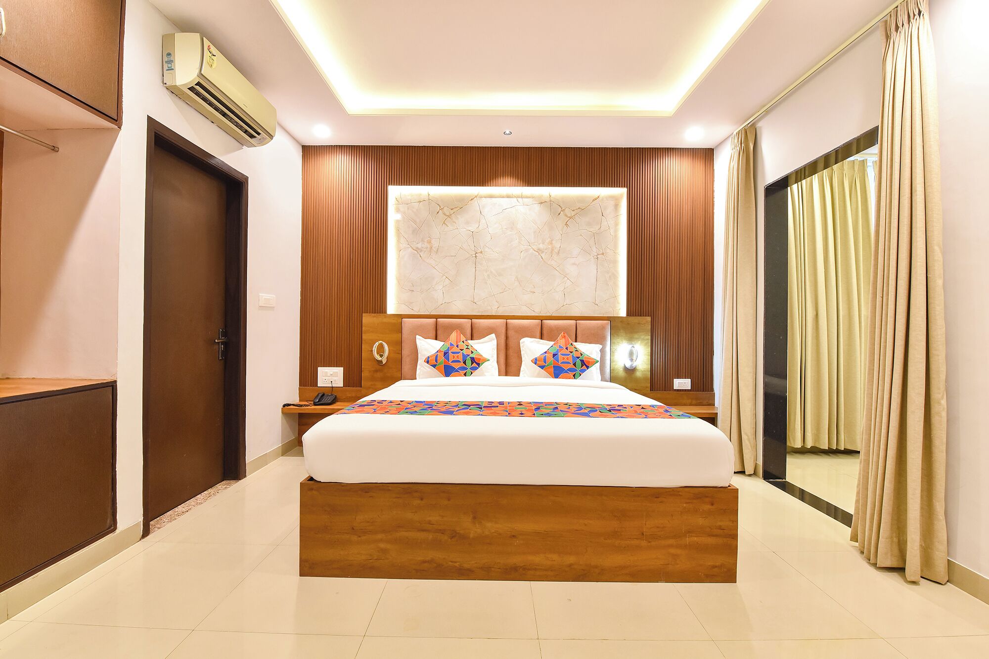 A hotel room with a large bed, a wooden headboard, a nightstand, a telephone, and a wall-mounted air conditioner.