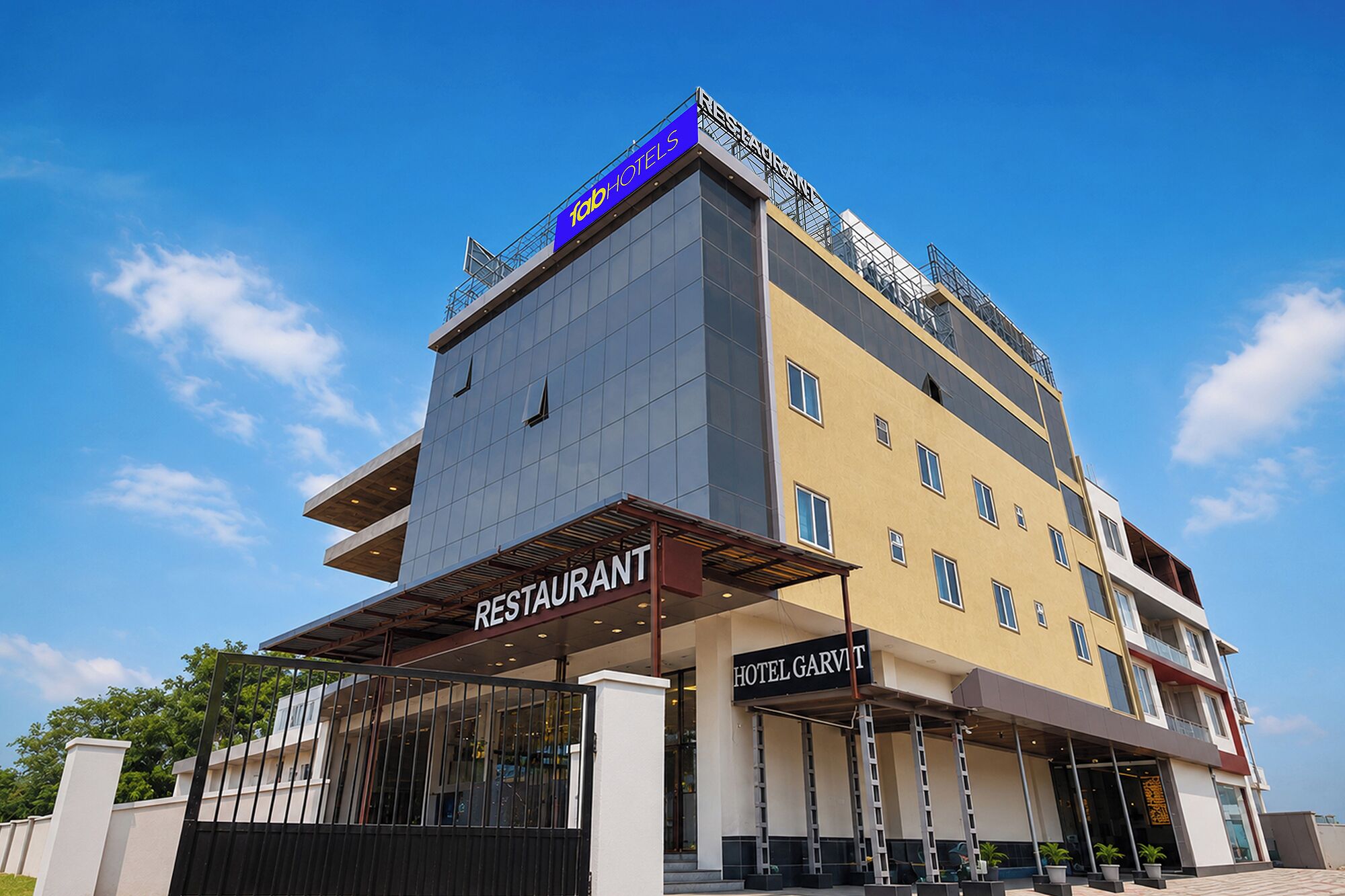 Um hotel de vários andares com restaurante no andar térreo, entrada visível e céu claro.