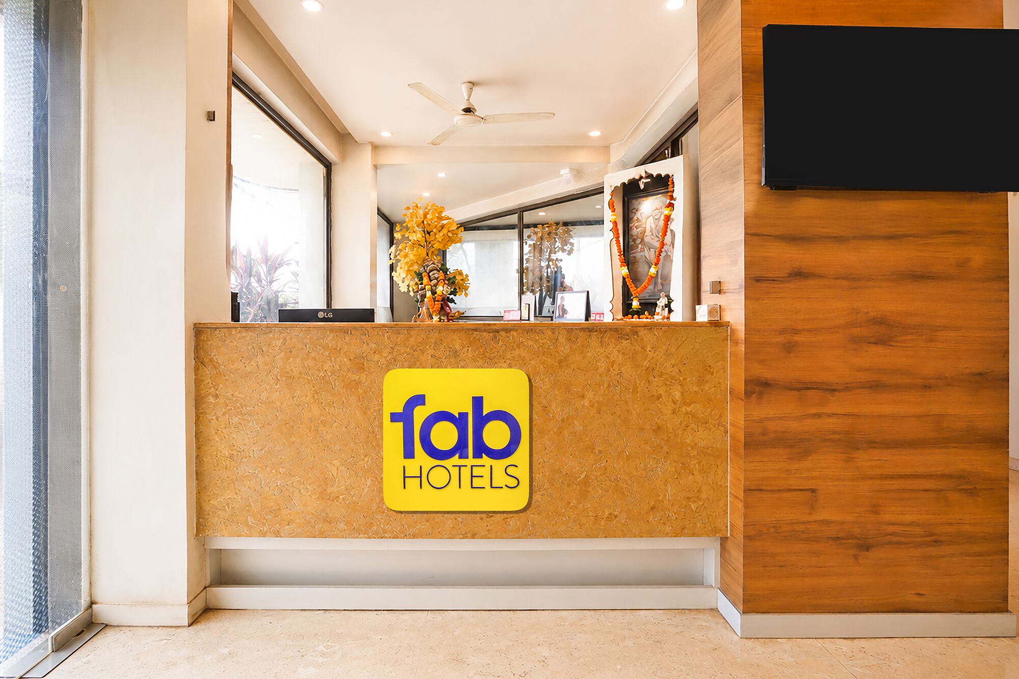 Una recepción con el r ótulo de Fab Hotels, un ventilador de techo y un panel de madera en la pared.