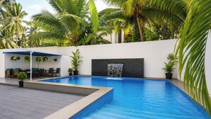 A swimming pool with a waterfall feature, surrounded by palm trees and a covered seating area. - FabHotel Pontas Luxury Stay (Calangute)