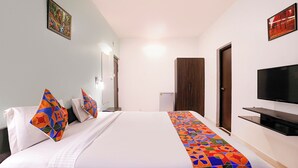 A hotel room with a bed, a television, a wardrobe, and a door. - FabHotel Pontas Luxury Stay (Calangute)