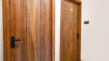 Dos puertas de madera con placas de latón, un pomo negro y un interruptor de luz en la pared.