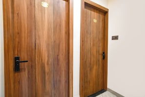 Two wooden doors with brass nameplates, a black door handle, and a light switch on the wall. - Fabhotel Ocean (Indore)