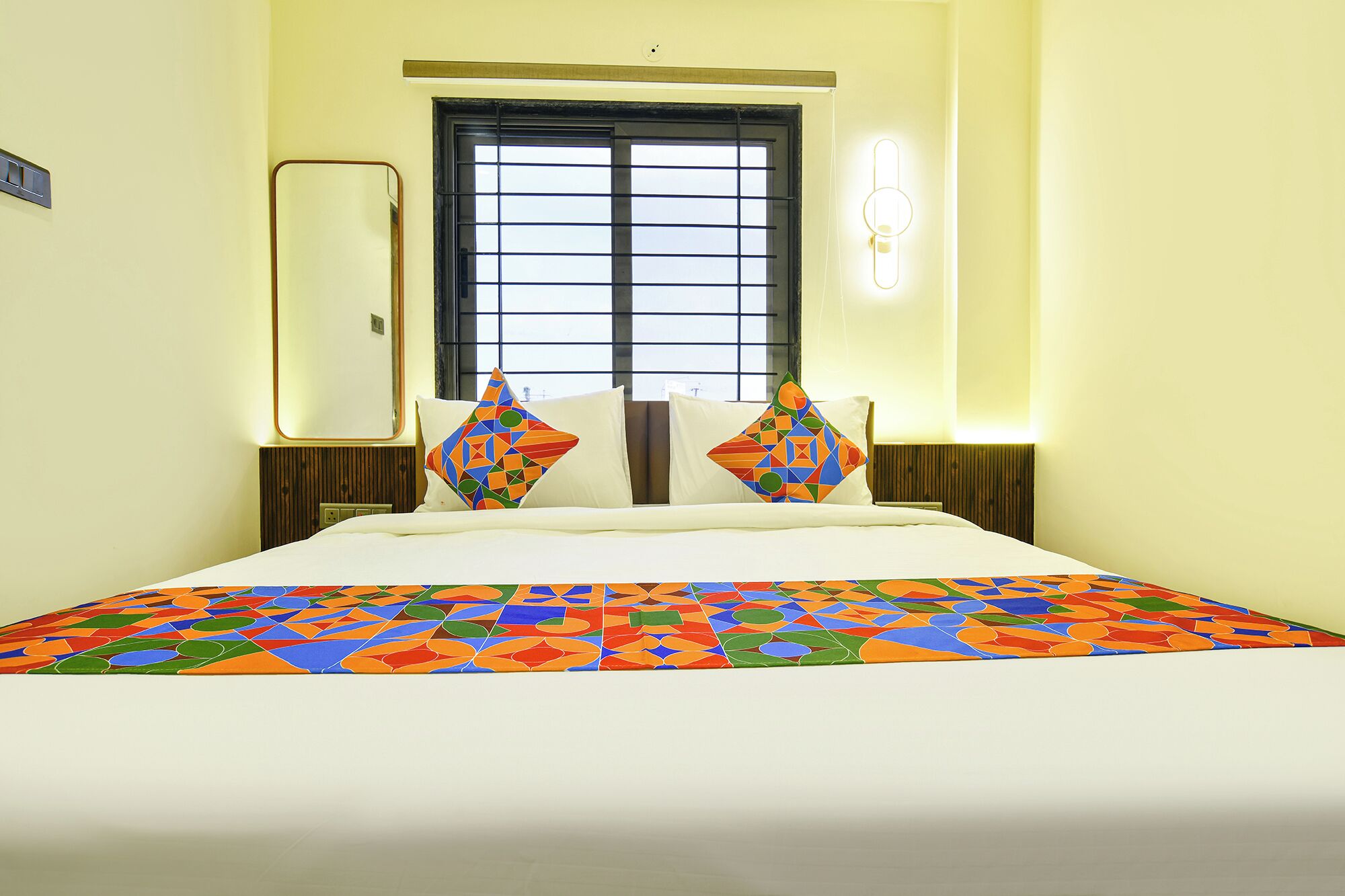 Habitación de hotel con cama, dos almohadas, ventana y una lámpara de pared.