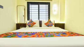 Habitación de hotel con cama, dos almohadas, ventana y una lámpara de pared.
