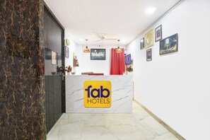 Zona de recepción de un hotel, con un mostrador de mármol, obras de arte enmarcadas en las paredes y un ventilador de techo.
