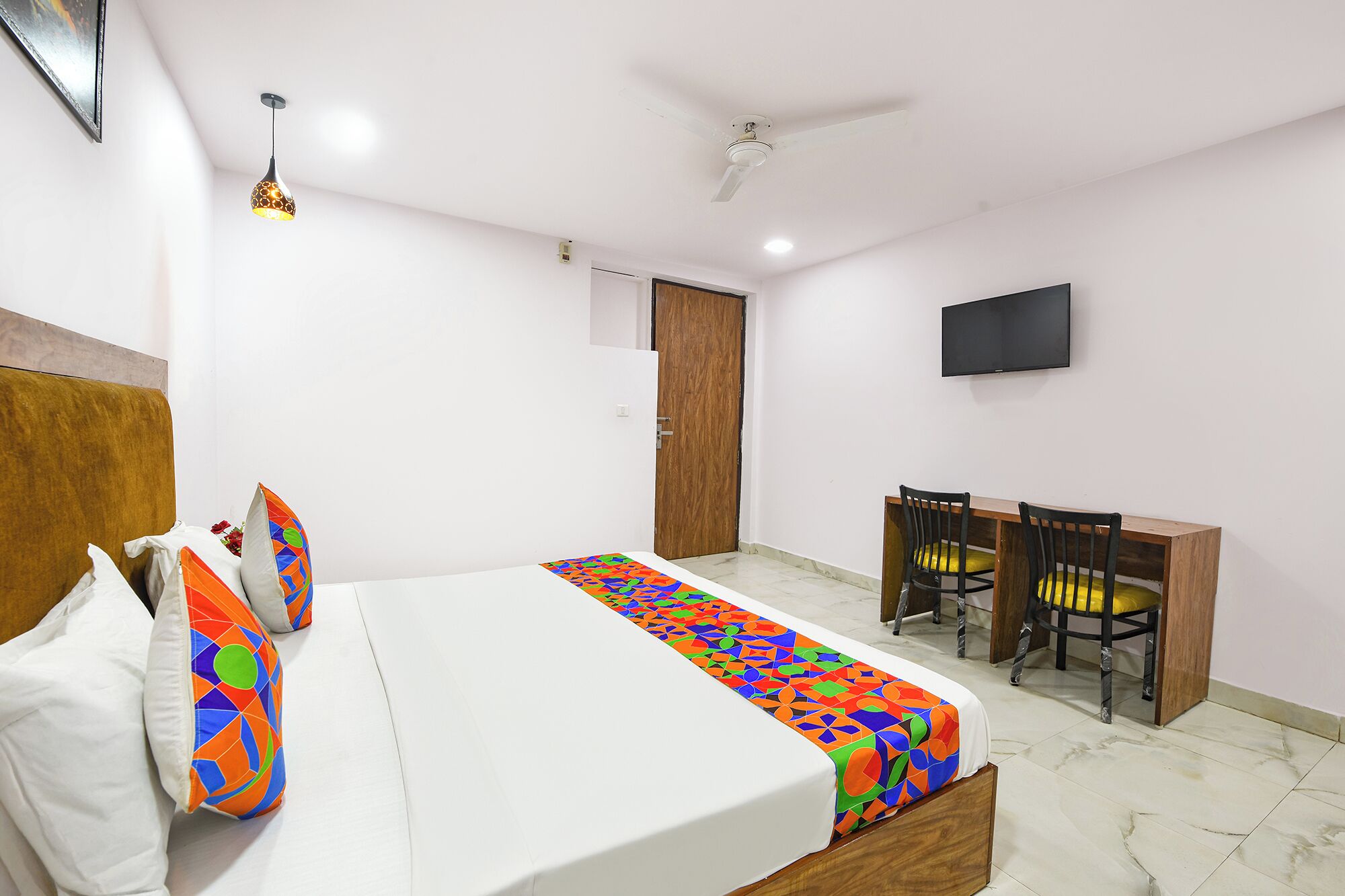 A hotel room with a bed, a desk, two chairs, a television, and a ceiling fan.
