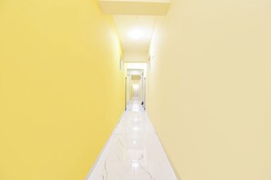 A corridor with a white floor and yellow walls, leading to a door at the end. - FabHotel Sattva Stays (Pune)