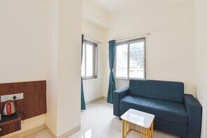 A room with a sofa, a small table, and a window with curtains. - FabHotel Sattva Stays (Pune)