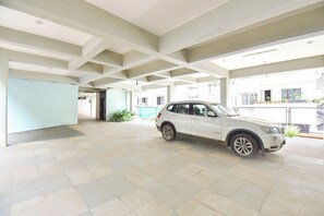 A spacious indoor area with a white SUV parked, a tiled floor, and a high ceiling with exposed beams. - FabHotel Sattva Stays (Pune)