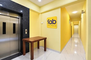 A hotel corridor with a sign for 'fab hotels', an elevator, and a wooden bench. - FabHotel Sattva Stays (Pune)