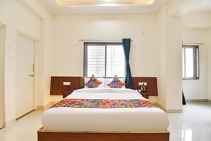 A hotel room with a large bed, a window with curtains, and a wooden headboard. - FabHotel Sattva Stays (Pune)