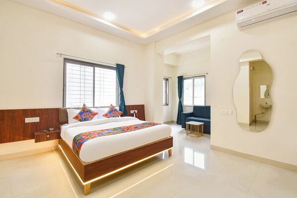 A modern hotel room with a large bed, bedside tables, a desk, and a mirror. - FabHotel Sattva Stays (Pune)
