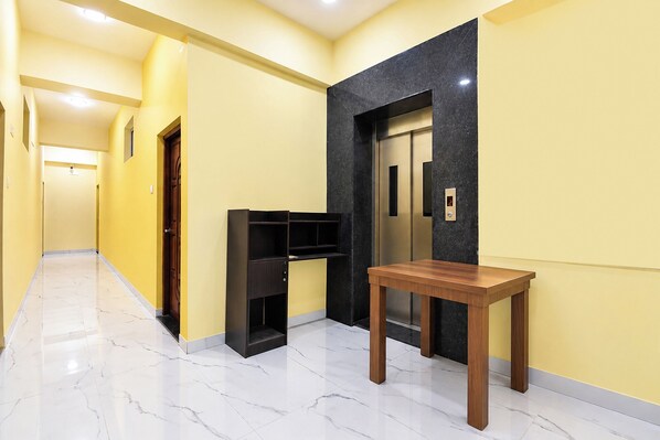 A hallway with a marble floor, a wooden table, a black shelving unit, and an elevator with a digital display. - FabHotel Sattva Stays (Pune)