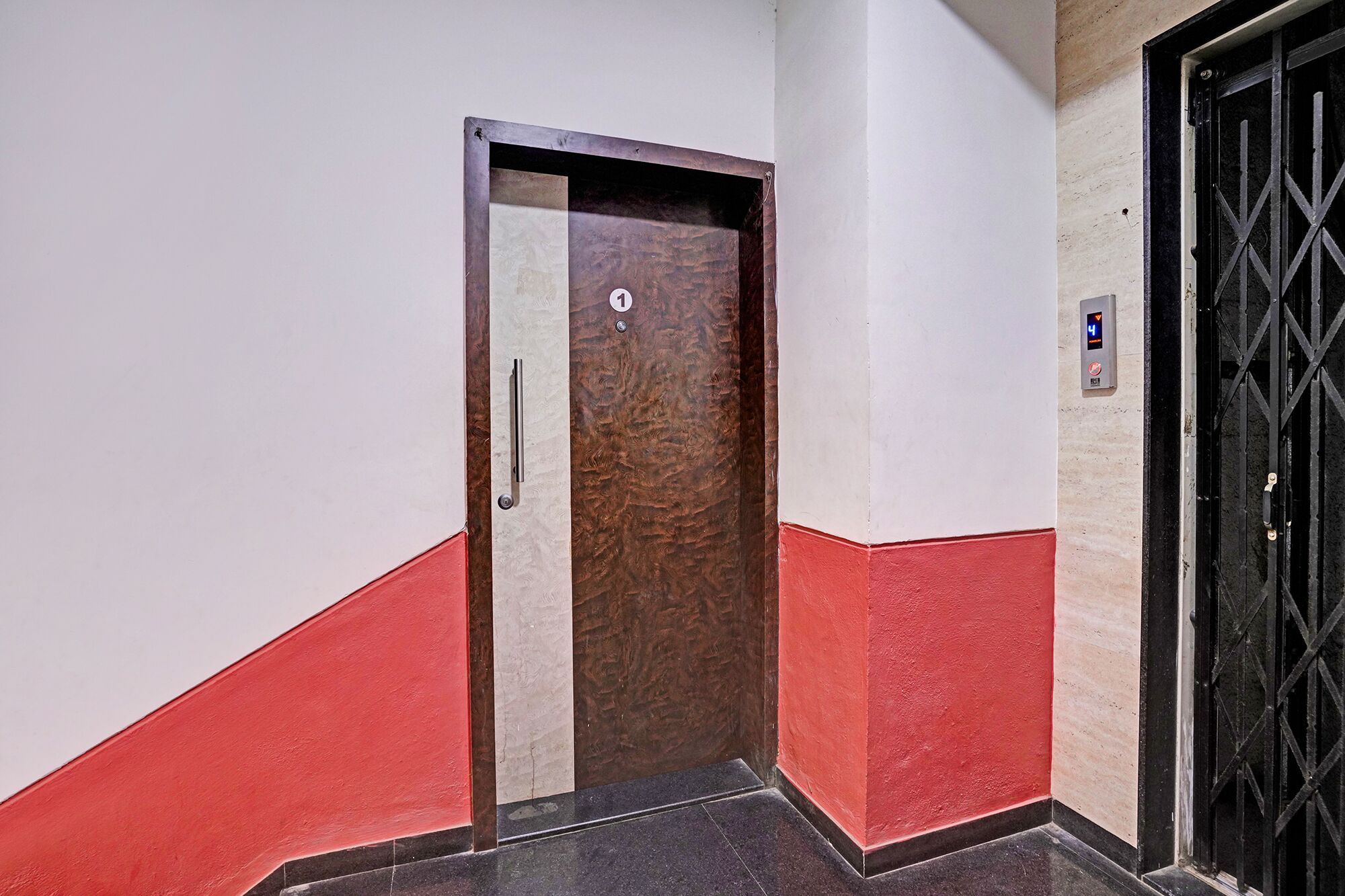 A hallway with a door marked with the number 1, a red and white wall, and a black metal gate on the right.