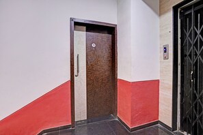 Un pasillo con una puerta numerada 1, una pared roja y blanca, y una reja metálica negra a la derecha.