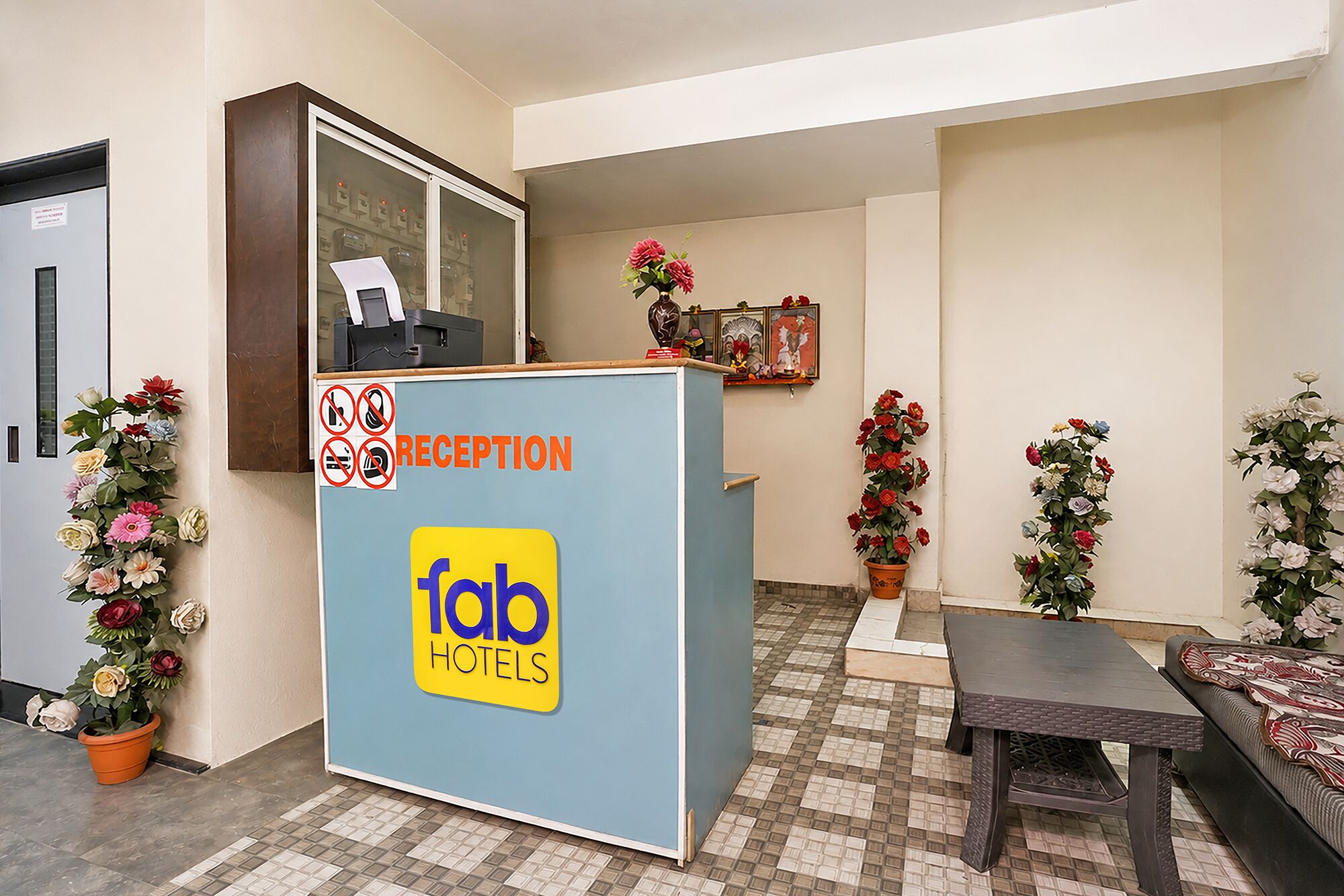 Una recepción con un cartel que dice 'fab hotels', un área de recepción con piso de baldosas y plantas en macetas.