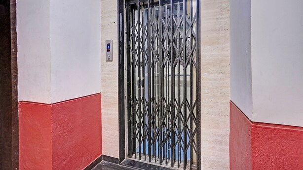 A hallway with a metal gate door, a wall-mounted control panel, and a red and white painted floor.