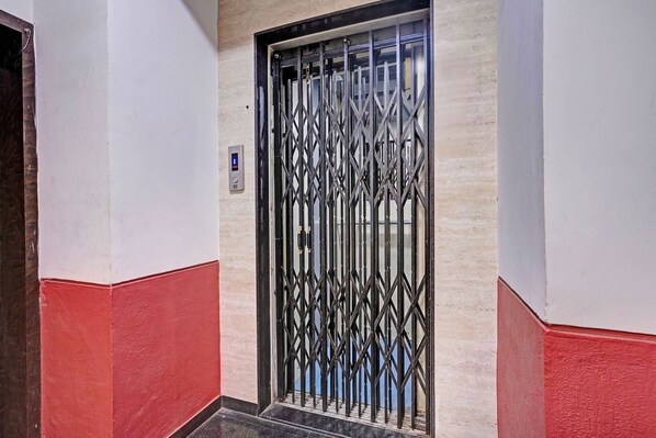 A hallway with a metal gate door, a wall-mounted control panel, and a red and white painted floor.