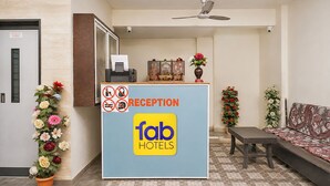 A reception desk with a 'fab hotels' sign, a ceiling fan, and a reception area with a sofa and decorative plants.