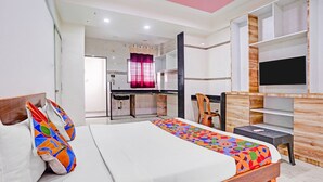 A hotel room with a bed, a desk, a TV, and a view of the kitchen.