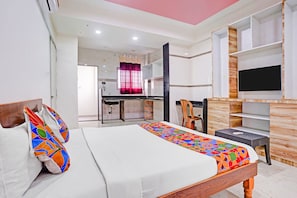 A hotel room with a bed, a desk, a TV, and a view of the kitchen.