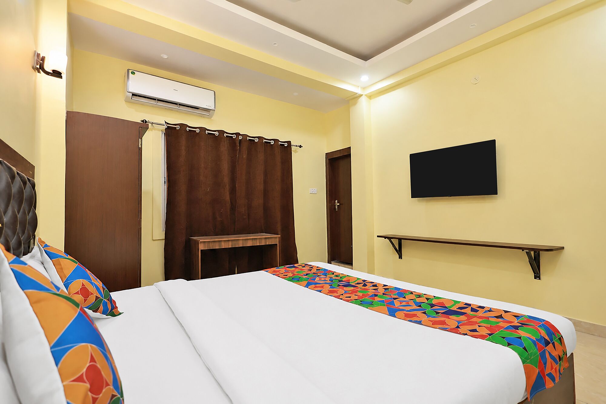 A hotel room with a bed, a TV, an air conditioning unit, and a curtain.
