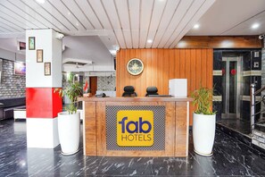 En hotellreception med en träpanel, en klocka och två krukväxter.