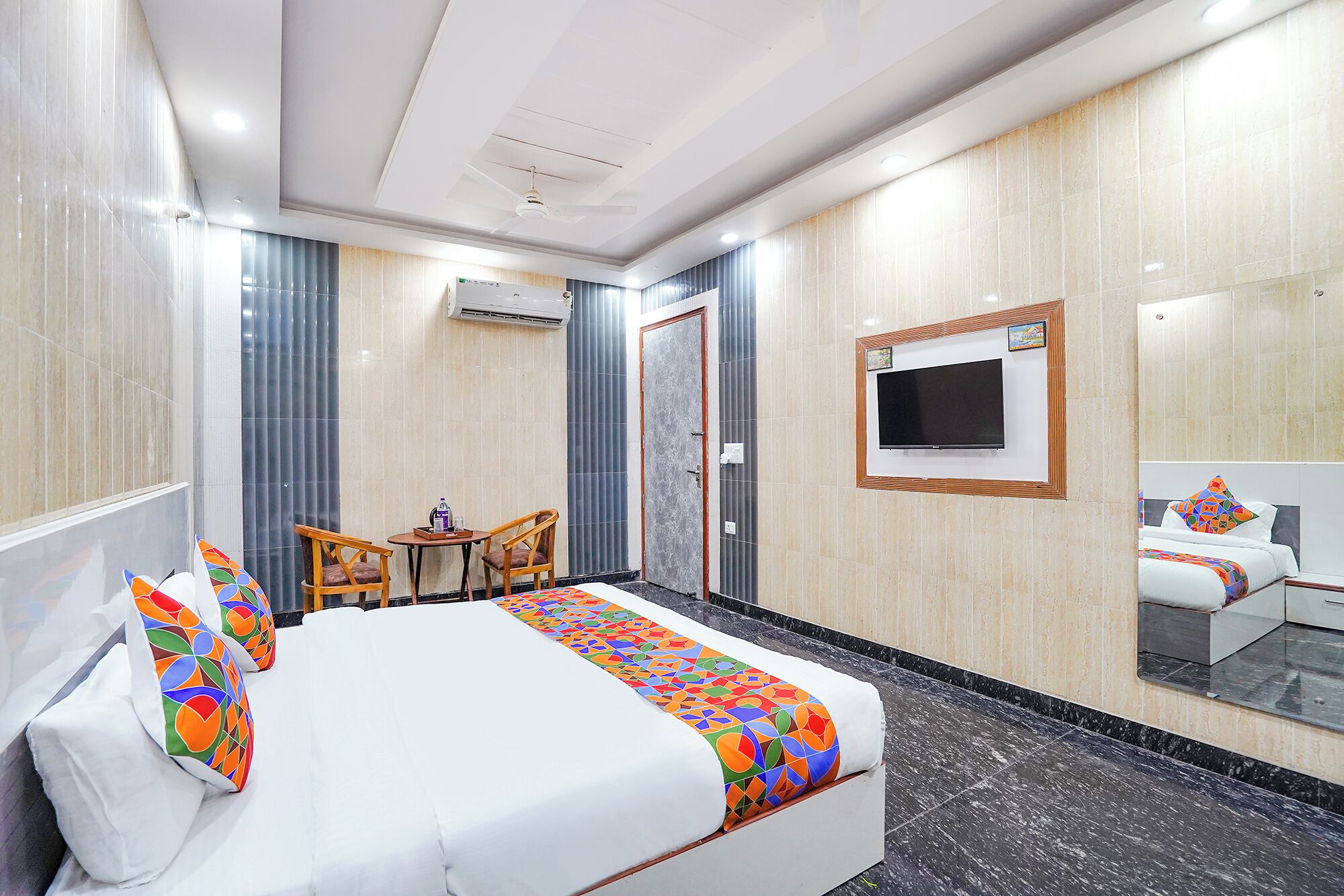 A hotel room with a bed, a TV, a small table with chairs, and a window with curtains.