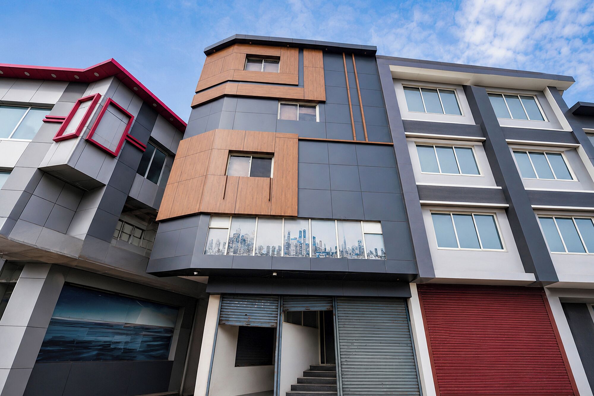 A multi-story building with a modern architectural design, featuring a combination of grey and wooden paneling, large windows, and a cityscape mural on the facade.