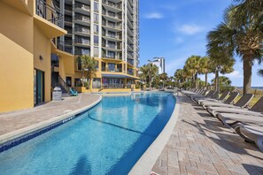 A swimming pool with lounge chairs, a multi-story building with balconies, and palm trees. - 1 BR Oceanfront Pet Friendly Fall Upgrades! (Myrtle Beach)