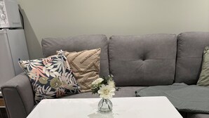 Une table basse blanche ornée d’un vase de fleurs, un canapé gris et un coussin à motifs.