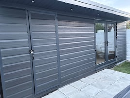 A modern building with horizontal siding, a sliding glass door, and a small patio area.