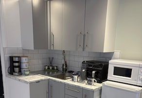 A modern kitchen with grey cabinets, a marble countertop, a coffee maker, a kettle, and a microwave.