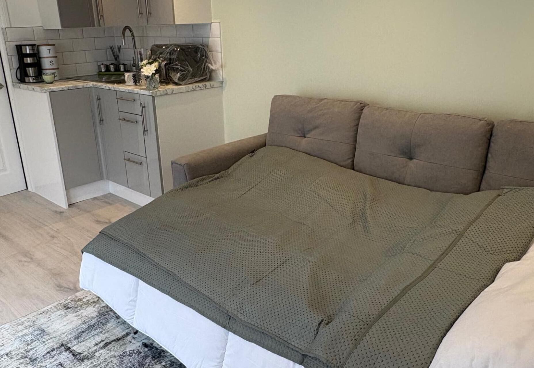 Een slaapkamer met een groot bed, een kleine kitchenette en een grijze bank.