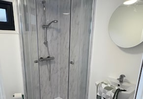 A bathroom with a marble shower enclosure, a sink, and a mirror.