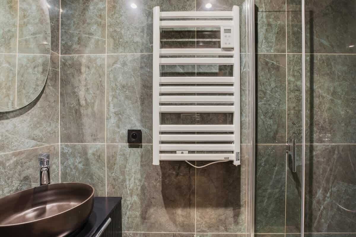 A bathroom with a marble floor, a white towel warmer, a sink with a modern faucet, and a glass shower enclosure.