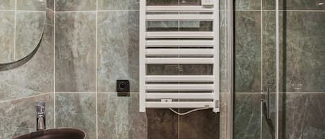 A bathroom with a marble floor, a white towel warmer, a sink with a modern faucet, and a glass shower enclosure.