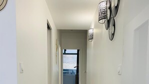 Un couloir doté d’un plancher en bois, de murs blancs et d’un luminaire au plafond.