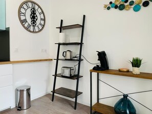 Eine Küche mit einem schwarzen Metallregal, einer Kaffeemaschine, einem Toaster und einer Wanduhr als Dekoration.