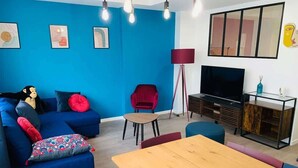 Un salon moderne avec un canapé bleu, une table à manger en bois et un téléviseur.
